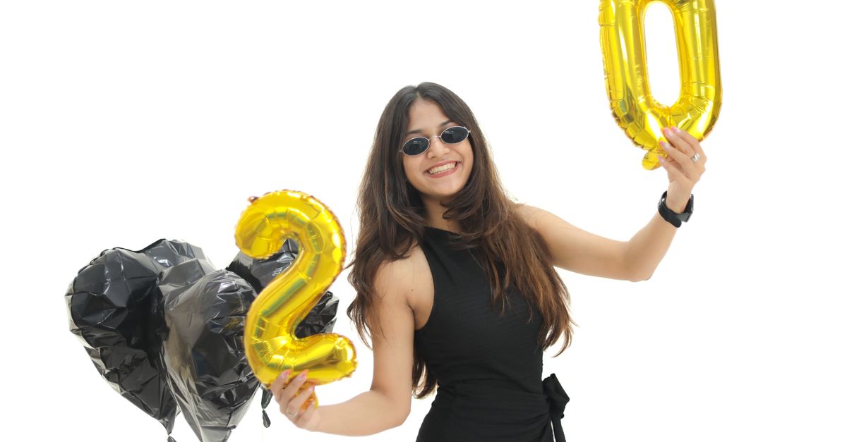 Smiling woman holding golden balloons for 2020, celebrating New Year with black heart balloons.